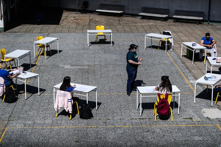 Des écoliers sont assis à des pupitres disposés en cercle en plein air à Buenos Aires