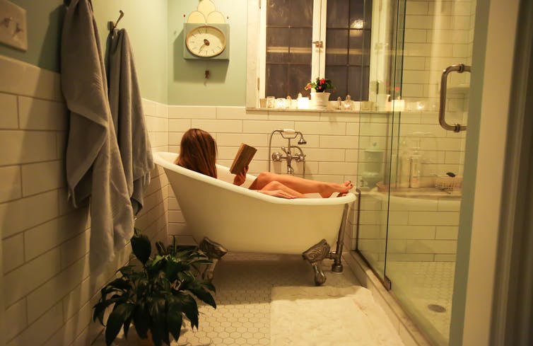 Femme lisant dans sa baignoire à la maison.